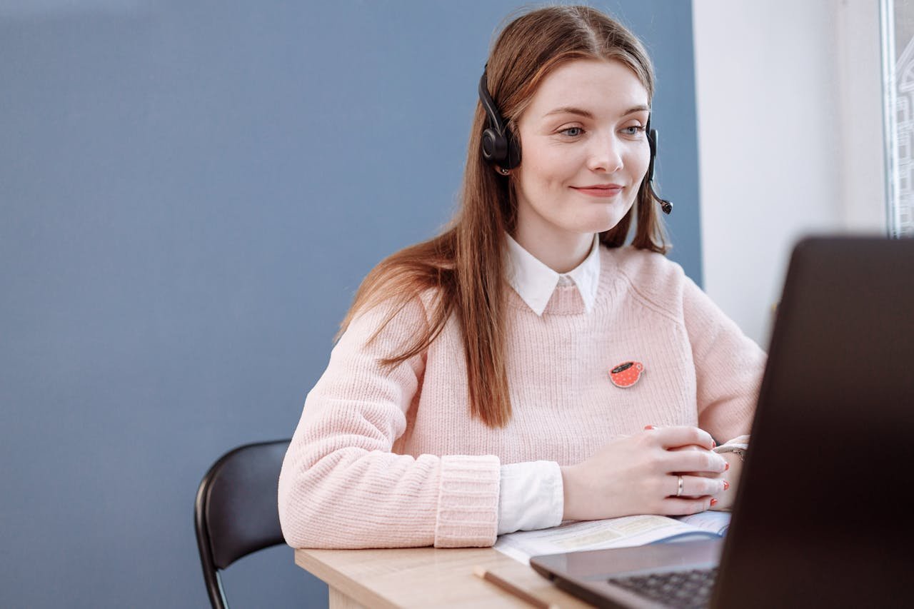 Smiling woman in pink sweater working remotely as a customer service agent.